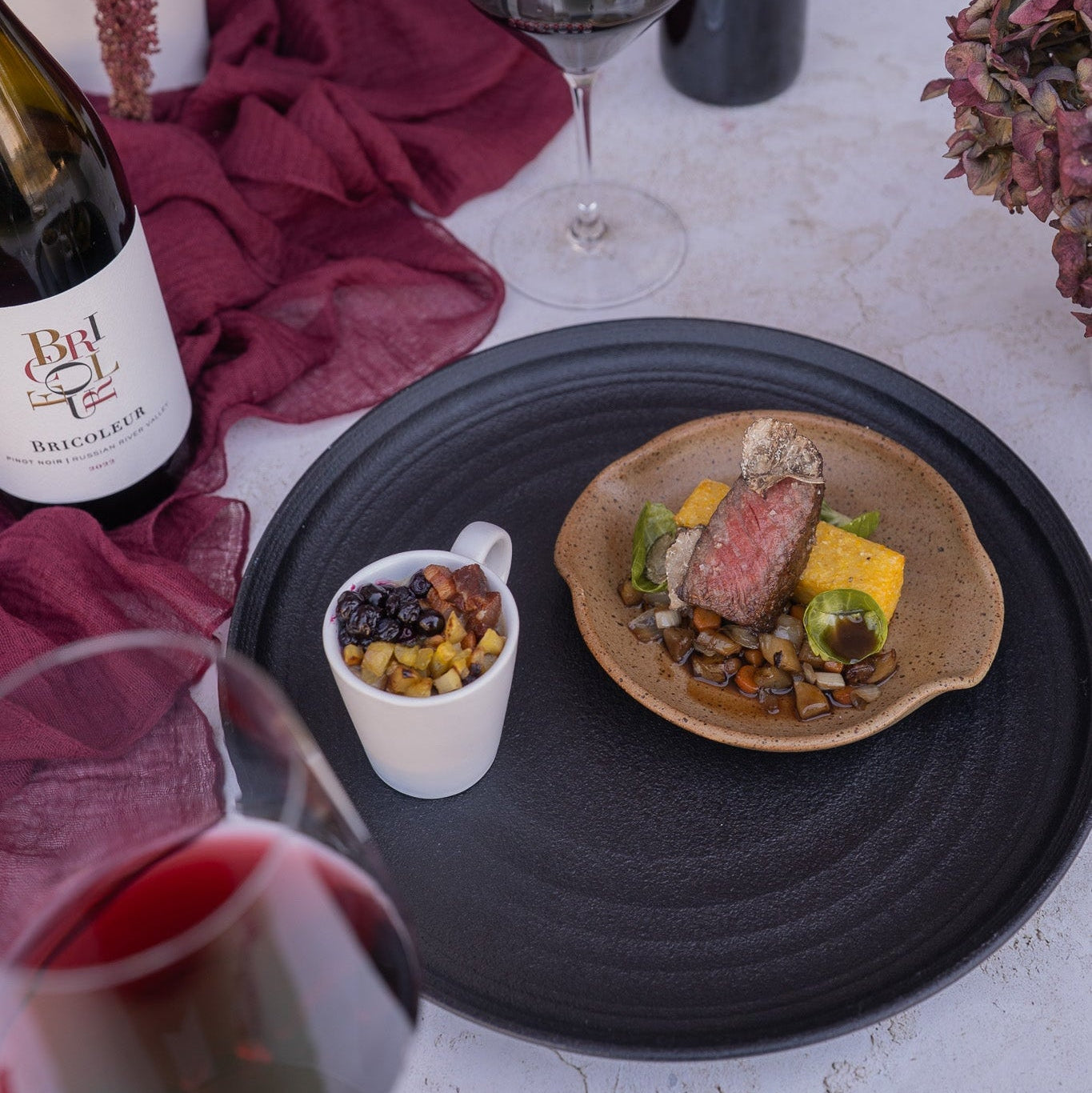 Dinner setting with a dish of food, wine glasses, and bottles on a table.